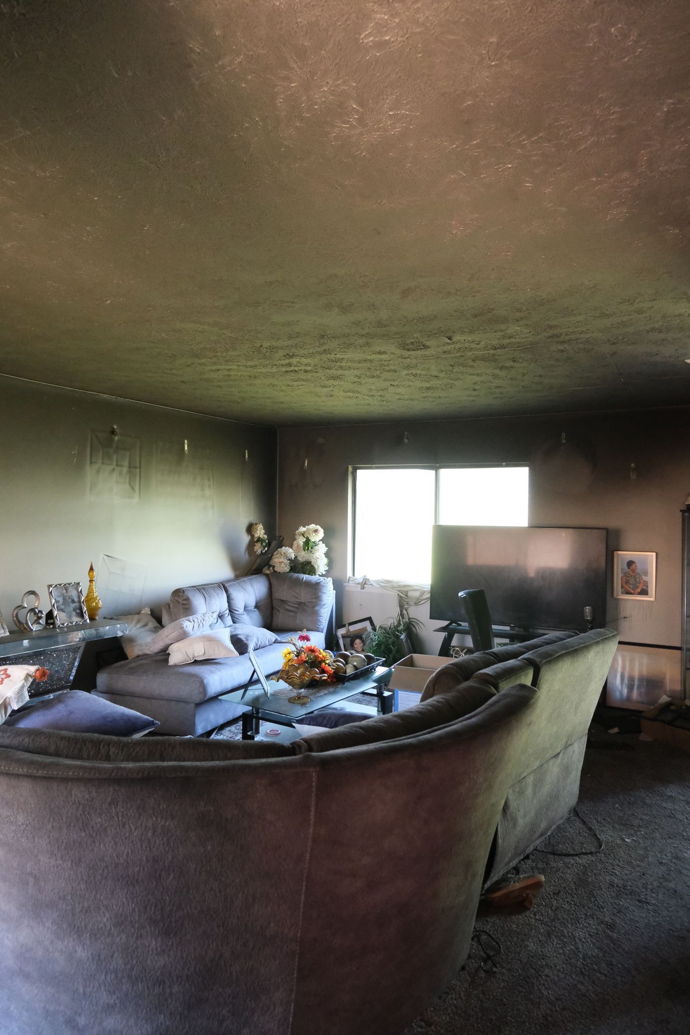 Living room interior heavily damaged by fire; charred walls and ceiling, ruined furniture.
