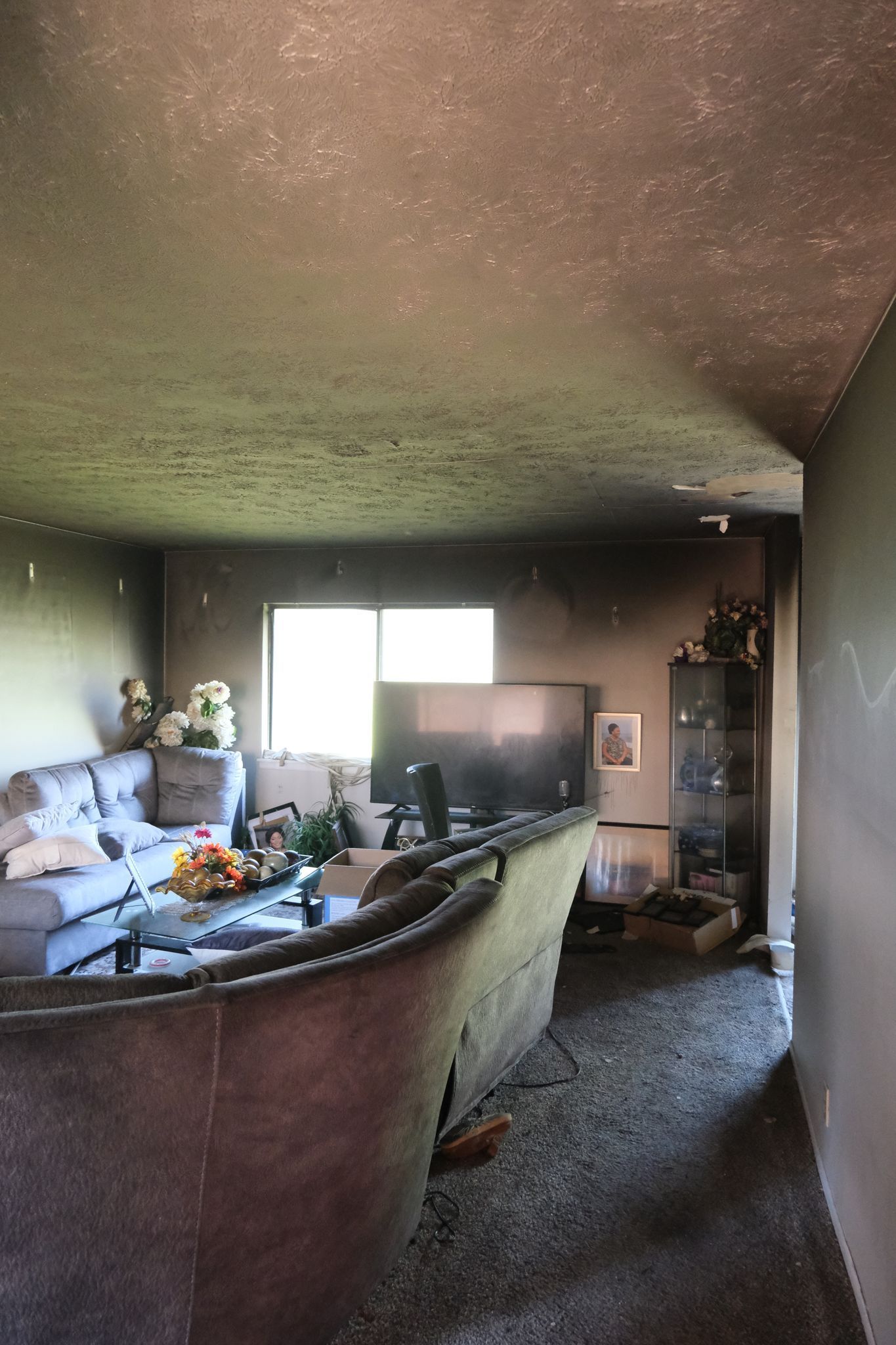 Living room heavily damaged by fire, walls and ceiling blackened, furniture charred.