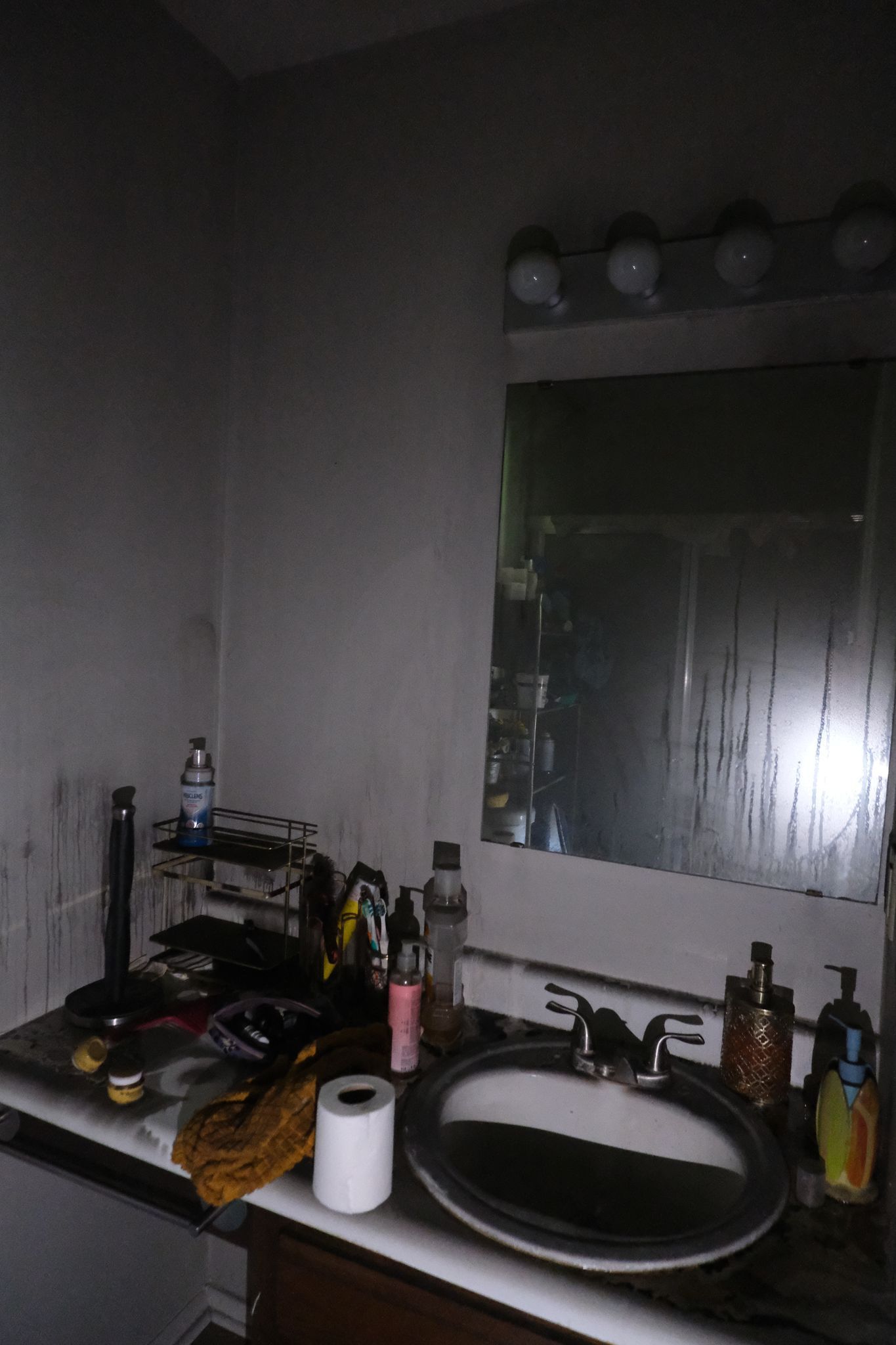 Bathroom with a countertop sink and mirror; items on the counter are charred and smoky, indicating fire damage.