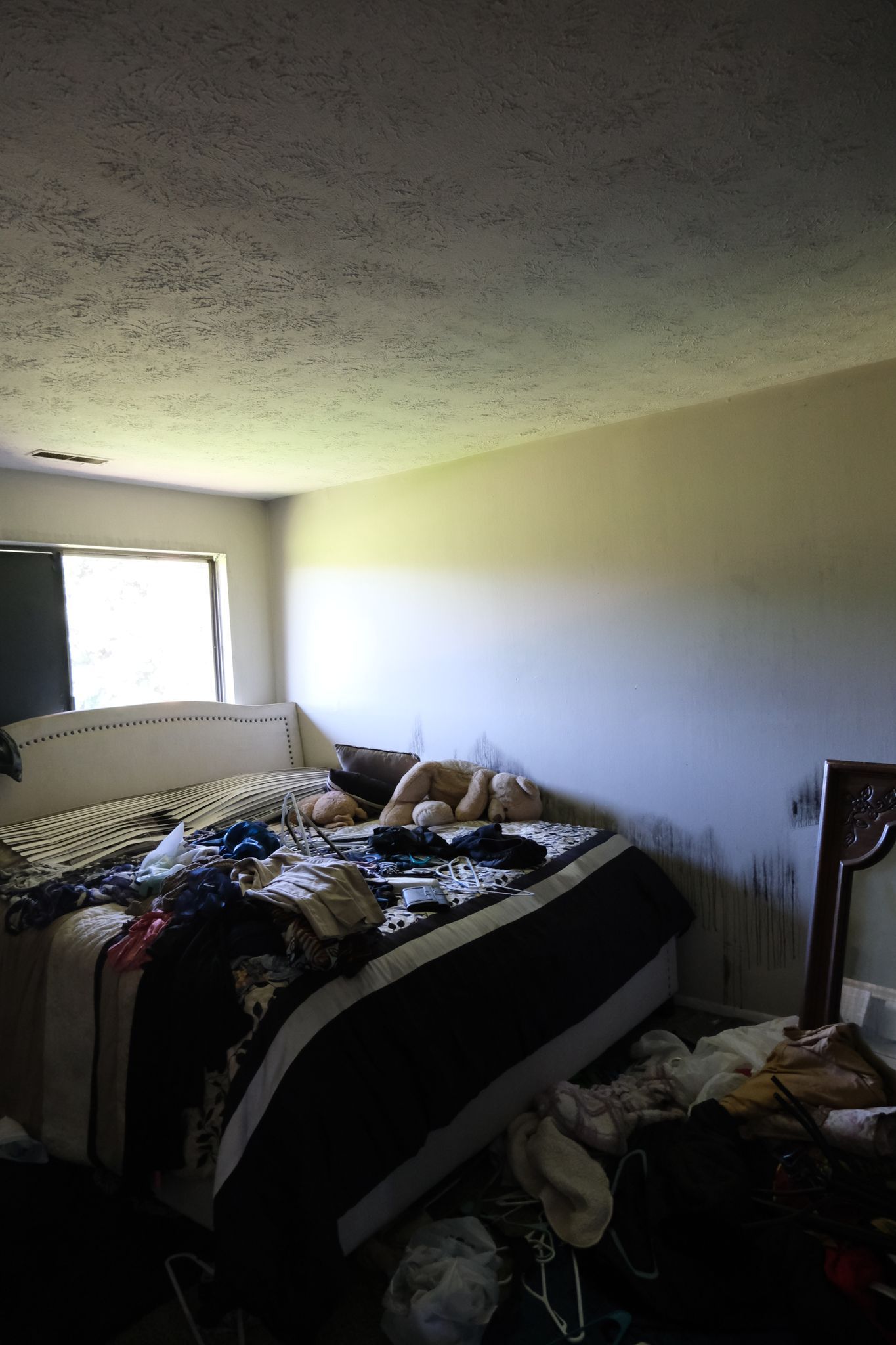 Messy bedroom with unmade bed, window, and clutter on the floor.