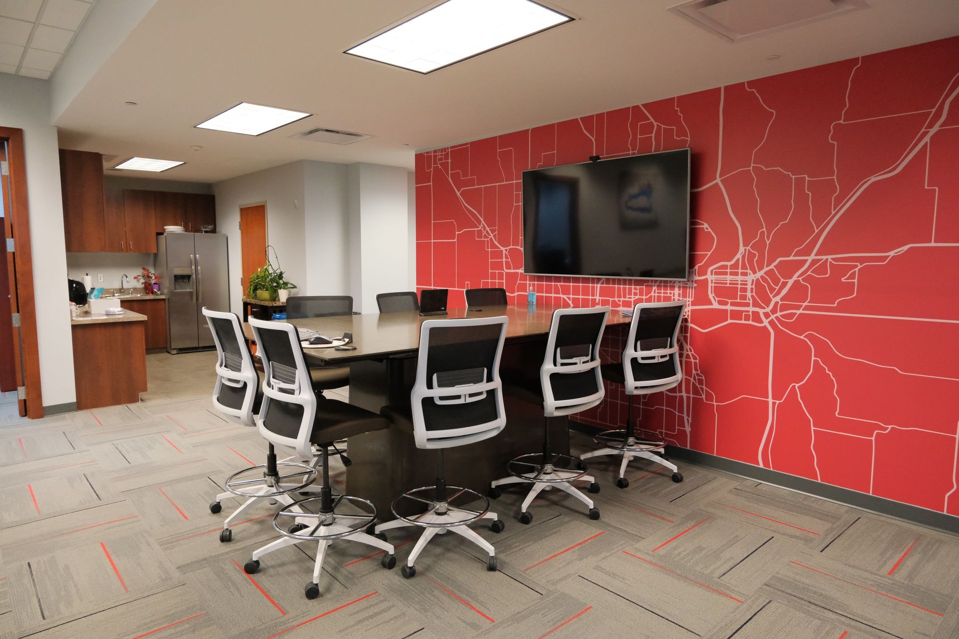 A conference room with a long table and chairs in front of a red wall.