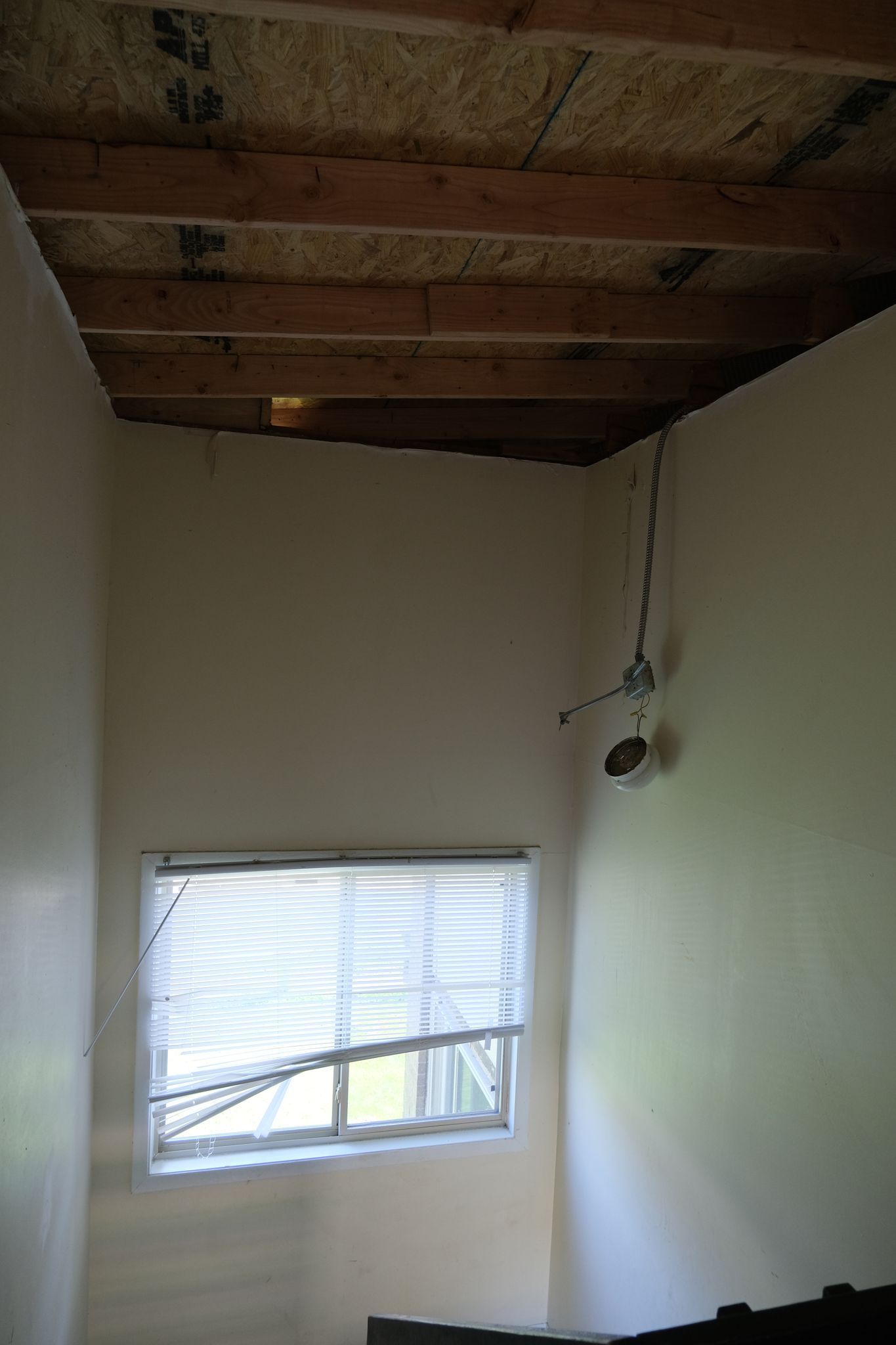 Interior of room with window, unfinished ceiling, electrical wires, and painted walls.