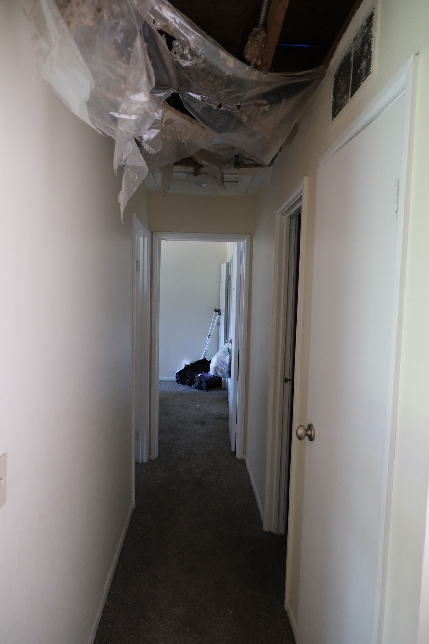 Narrow hallway with damaged ceiling and doors.