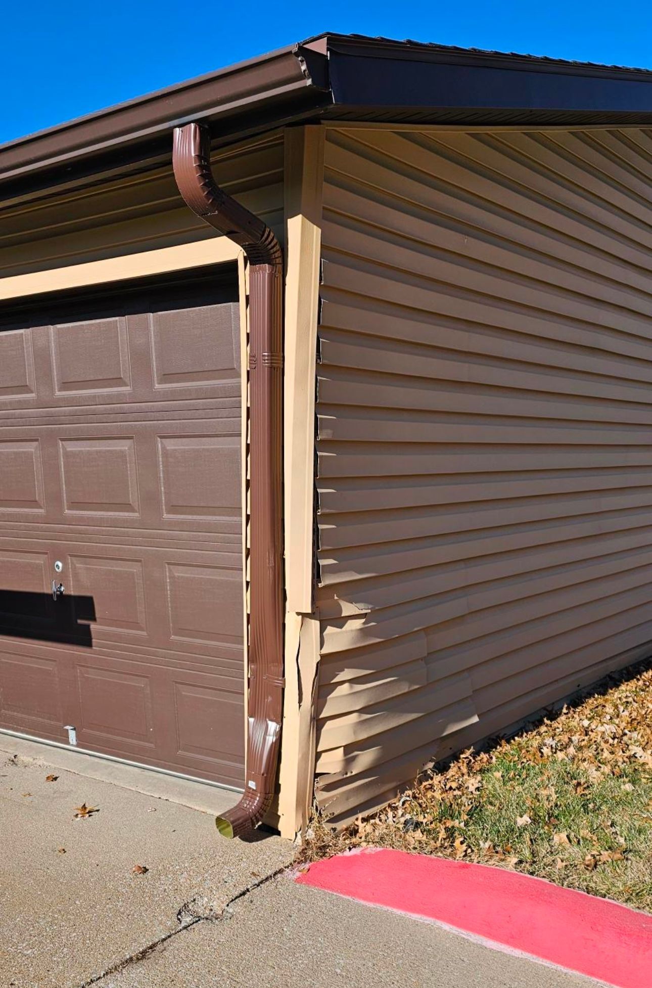 A garage with a brown door and a brown gutter on the side of it.