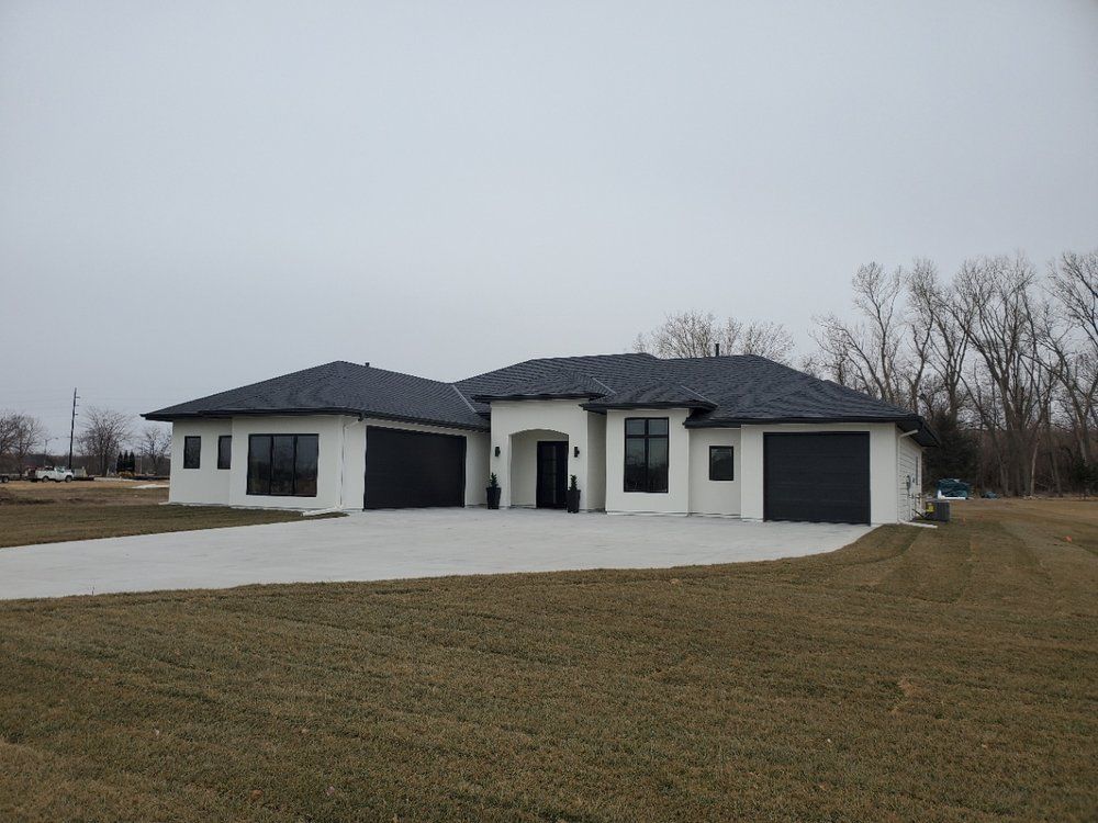 A large white house with a black roof is sitting in the middle of a grassy field.
