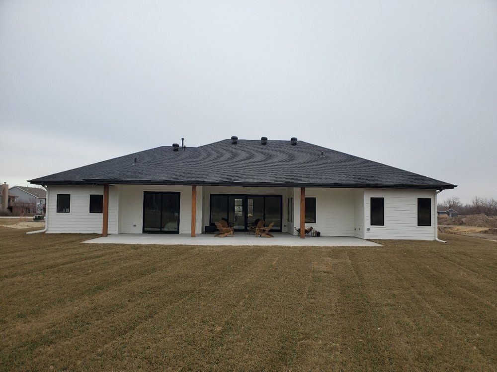 A large white house with a black roof is sitting in the middle of a grassy field.
