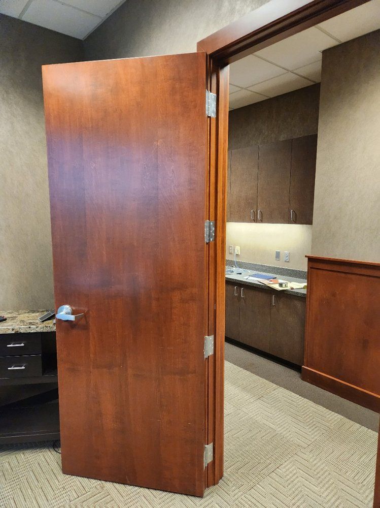 A wooden door is open in a room with a kitchen in the background.