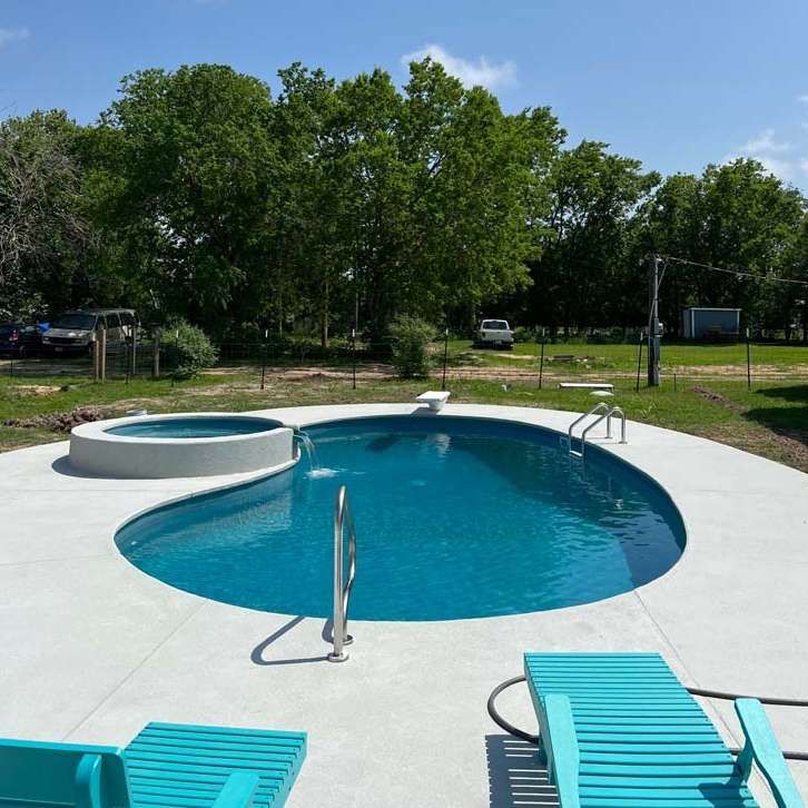 A large swimming pool with two blue chairs in front of it