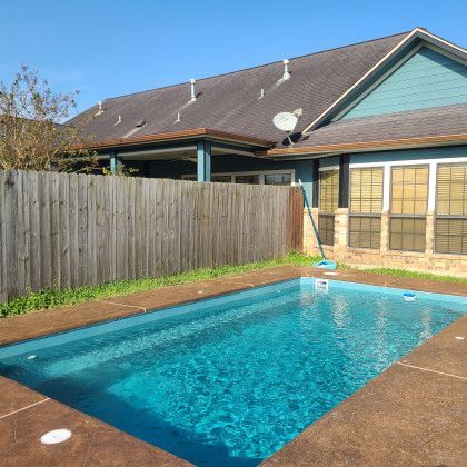 A large swimming pool in front of a house with a wooden fence.