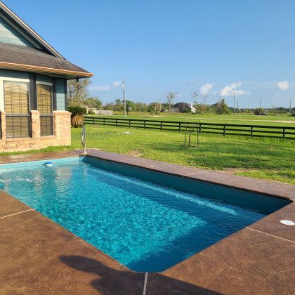 A large swimming pool in front of a house with a fence in the background.