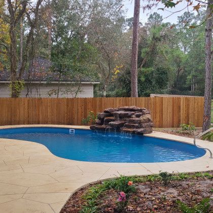 A large swimming pool with a waterfall in the backyard behind a wooden fence.