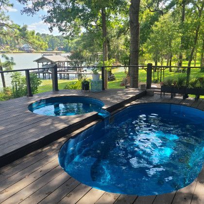 Two swimming pools are on a wooden deck next to a lake.