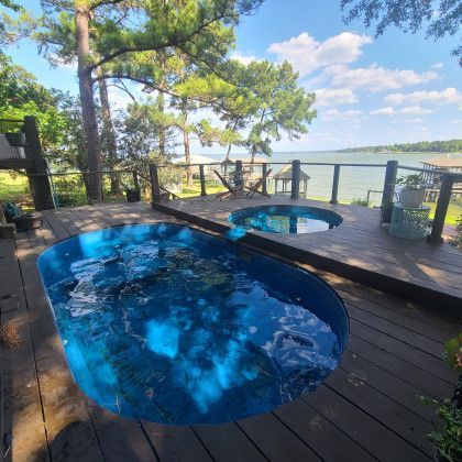 Two swimming pools are on a wooden deck overlooking a lake.