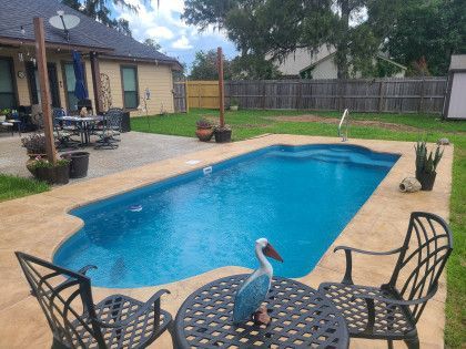A large swimming pool is surrounded by chairs and a table.