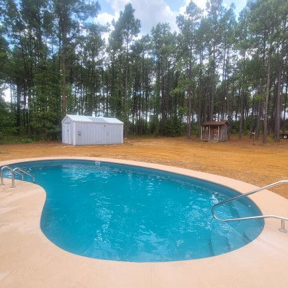 A large swimming pool is surrounded by trees and a shed.