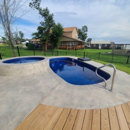 A swimming pool with a jacuzzi next to it and a house in the background.