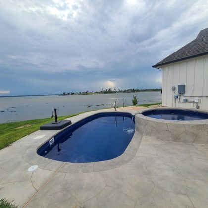 A large swimming pool with a hot tub next to a body of water.