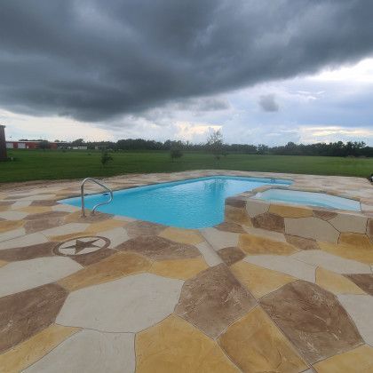 A large swimming pool is surrounded by a tiled patio on a cloudy day.