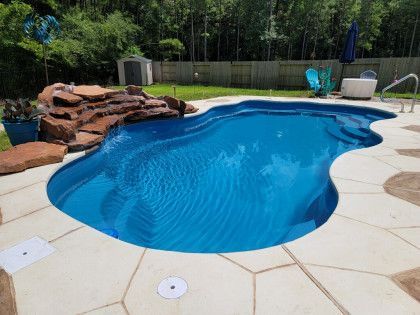 A large blue swimming pool with a waterfall in the backyard.