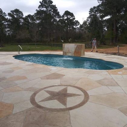 A man is standing next to a swimming pool with a waterfall in the background.