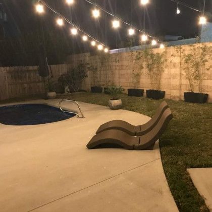 A backyard with a swimming pool and chairs at night