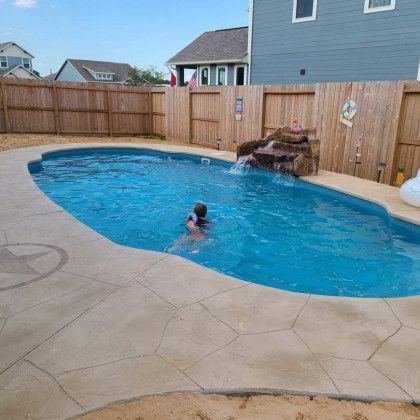 A child is swimming in a large swimming pool with a waterfall.