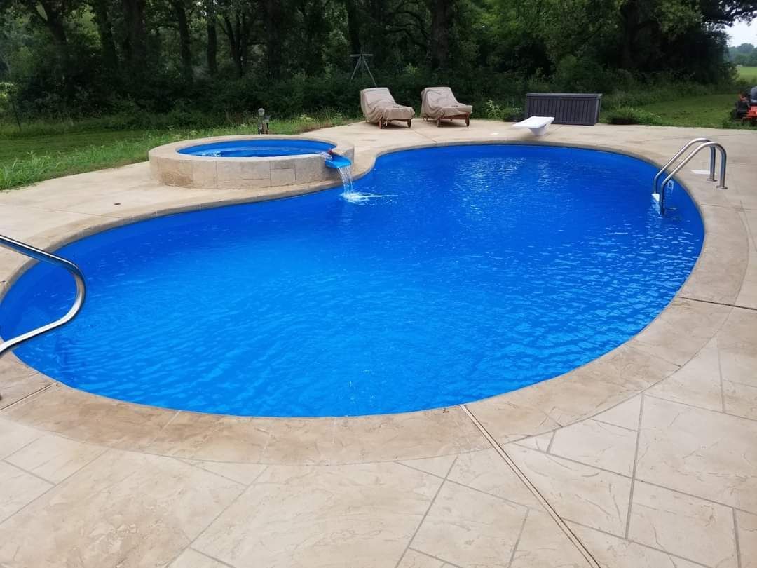 A large blue swimming pool with a hot tub in the backyard