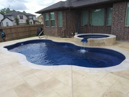 A large swimming pool with a hot tub in front of a brick house.