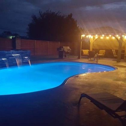 A large swimming pool is lit up at night with a waterfall.