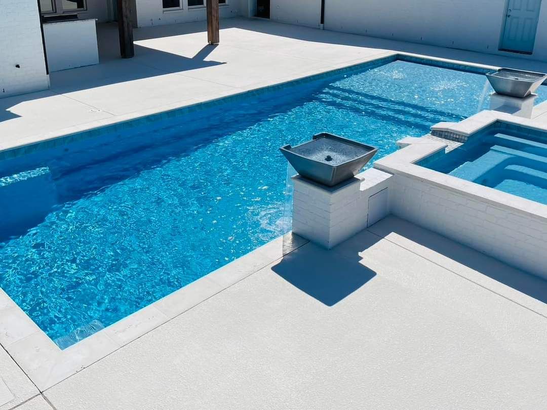 There is a large swimming pool in the backyard with chairs and umbrellas.