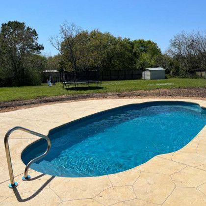 A large swimming pool with stairs leading to it in a backyard.
