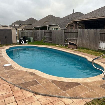 A large swimming pool is surrounded by a fence in a backyard.