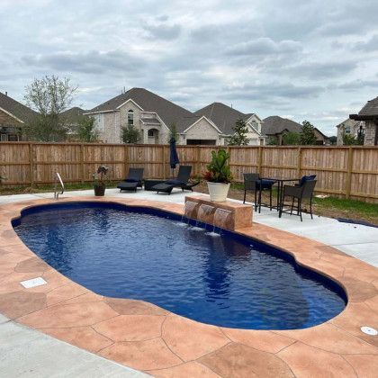 A large swimming pool with a waterfall in the backyard of a house.