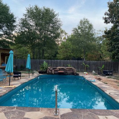 A large swimming pool surrounded by trees and umbrellas in a backyard.