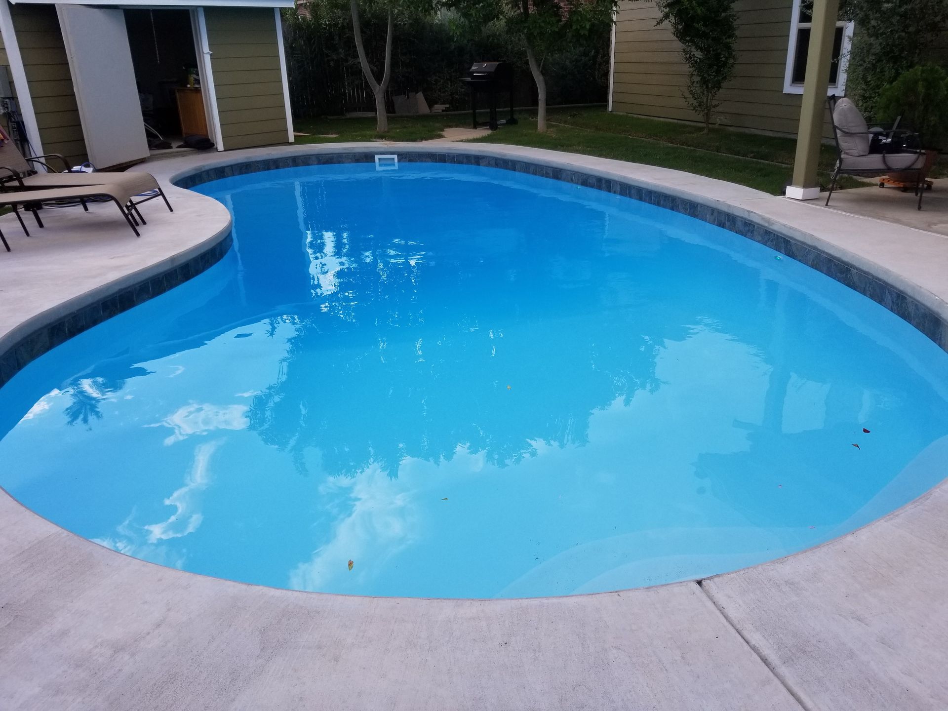 A large swimming pool with blue water in a backyard.