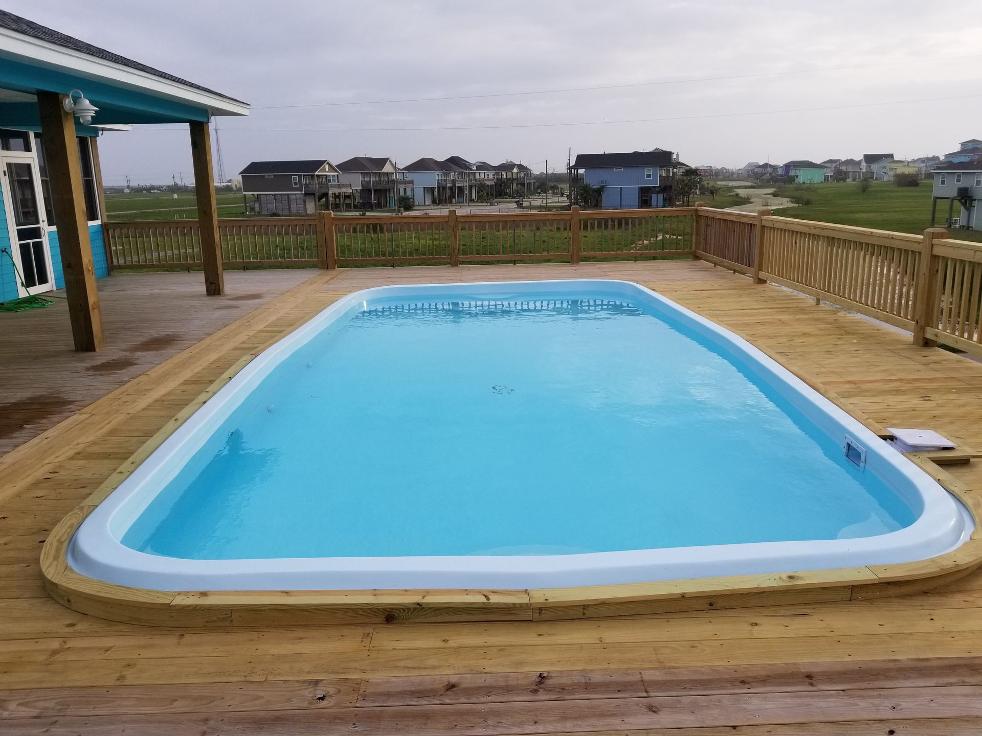 A large swimming pool is sitting on top of a wooden deck.