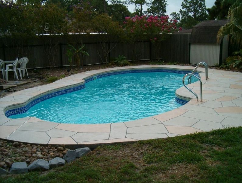 A swimming pool in a backyard with a table and chairs in the background