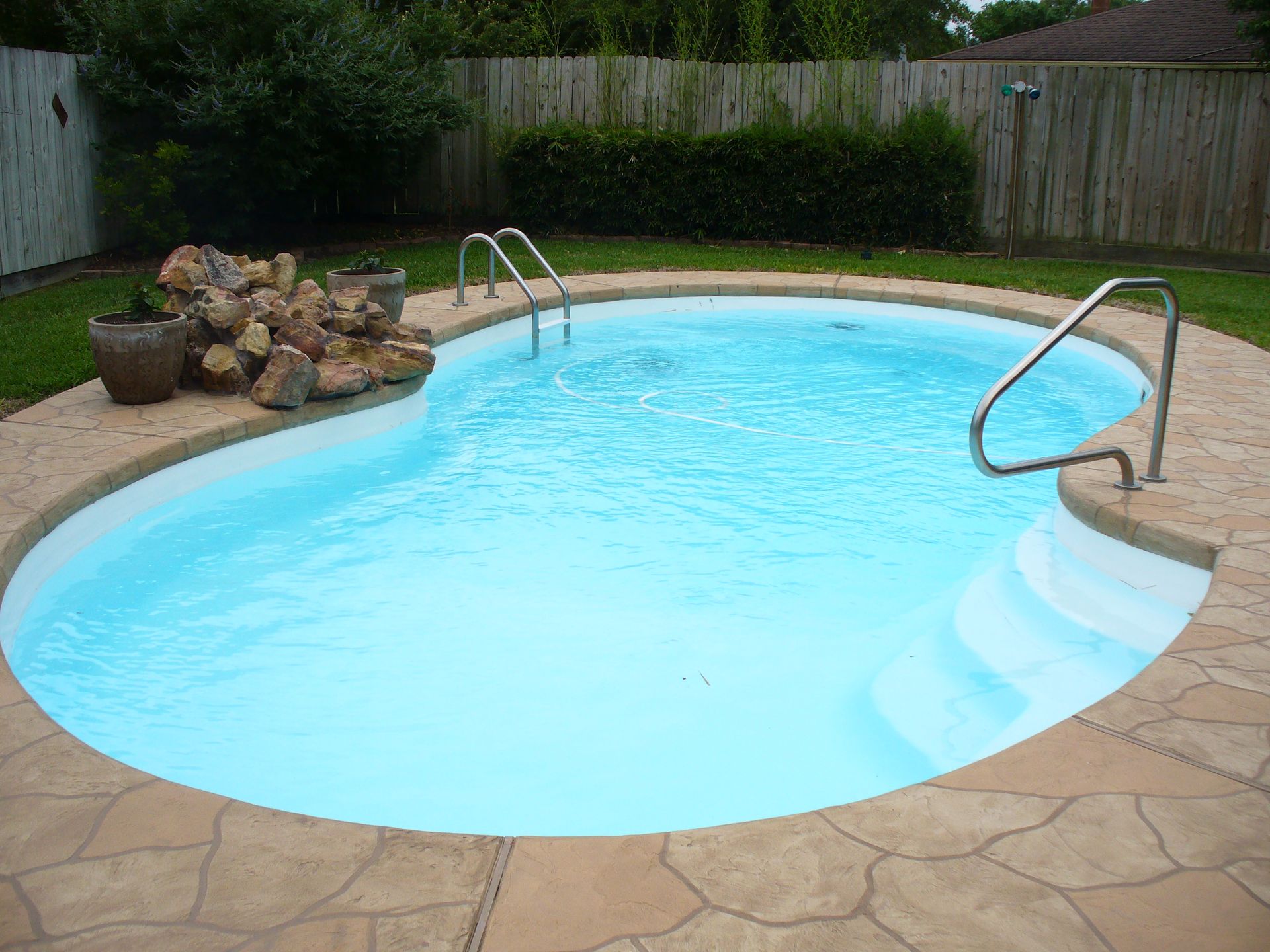 There is a large swimming pool in the backyard with a fence around it.