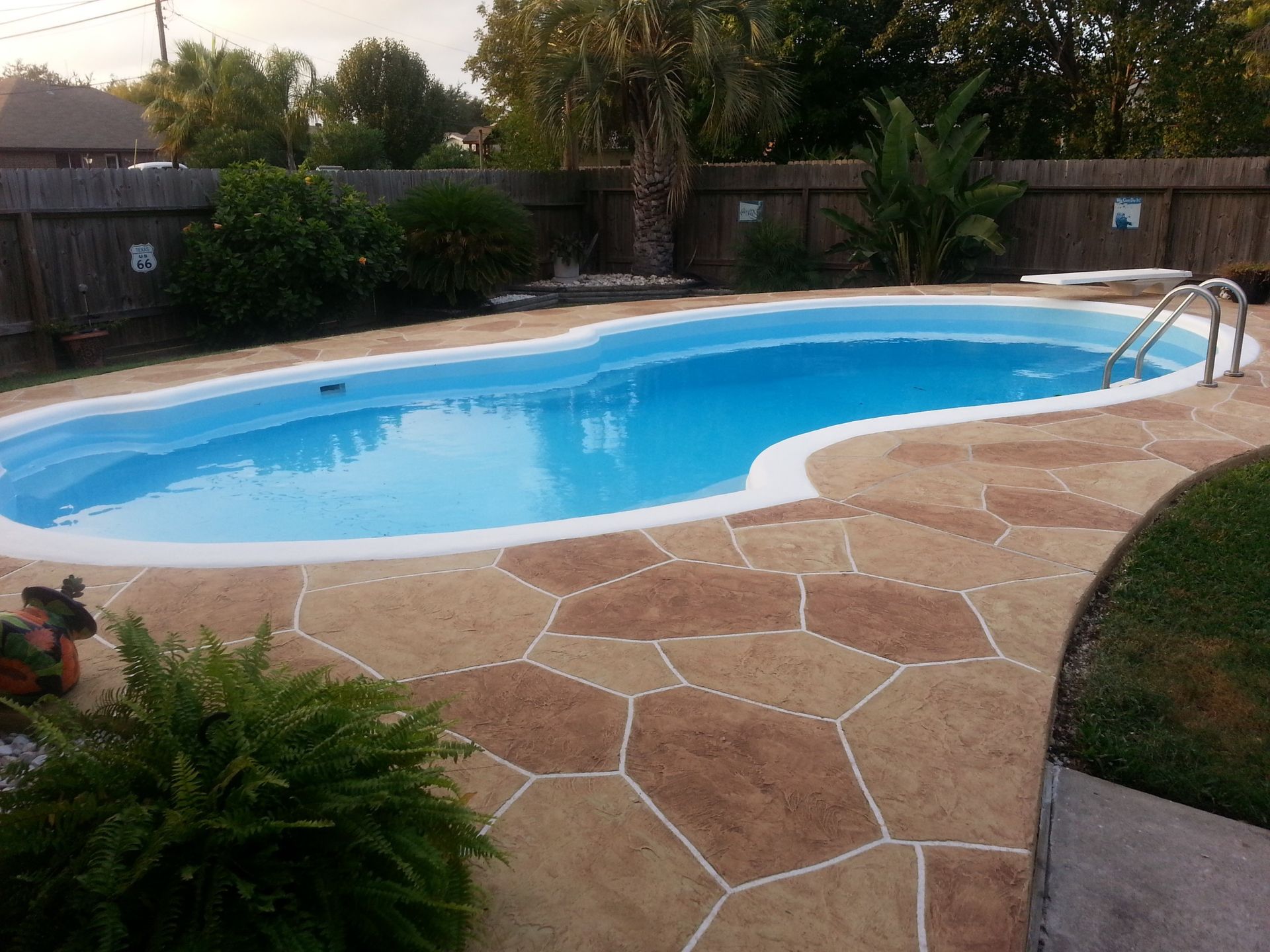 A large swimming pool is surrounded by a fence and a patio.