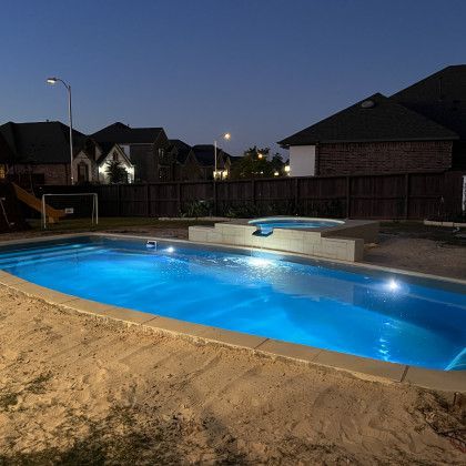 A large swimming pool is lit up at night in a backyard.