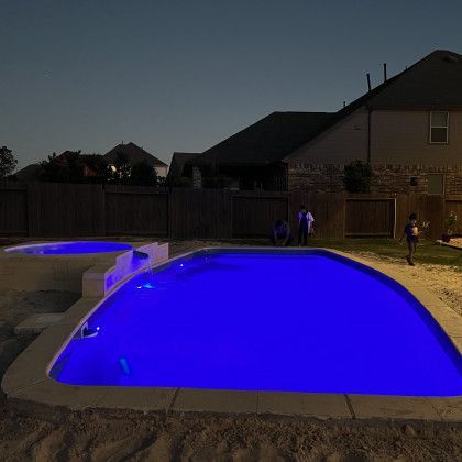 A large swimming pool is lit up with blue lights at night.