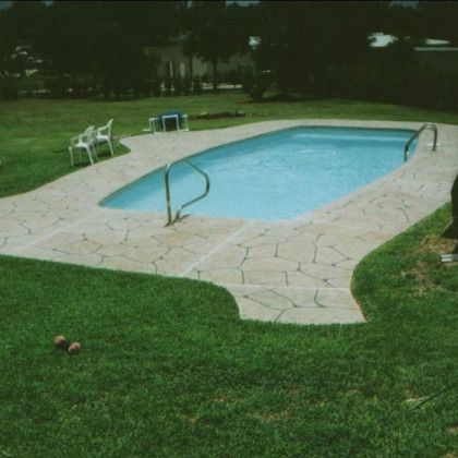 A large swimming pool is surrounded by grass and chairs