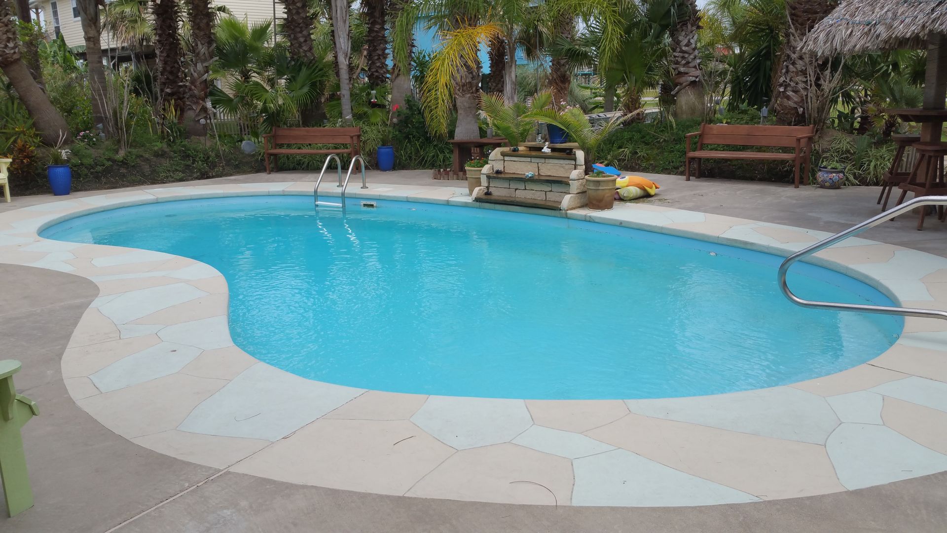 There is a large swimming pool in the middle of a garden.