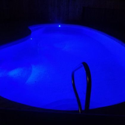 A large swimming pool is lit up with blue lights at night.