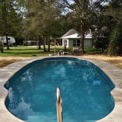 A large swimming pool is surrounded by trees and a house in the background.