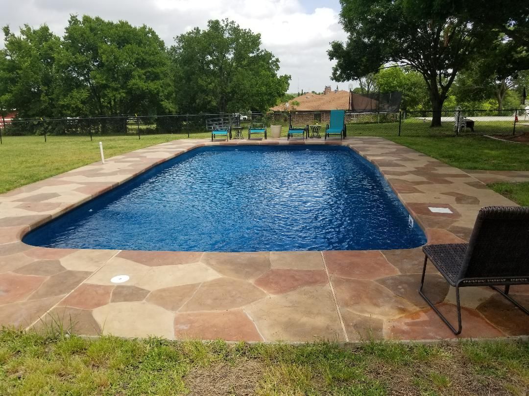 A large swimming pool is surrounded by a stone patio.