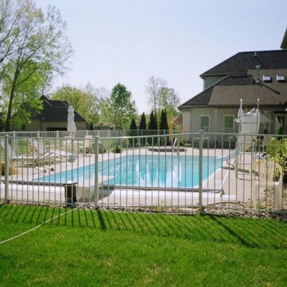 A fence surrounds a large swimming pool in front of a house