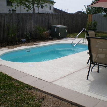 A swimming pool in a backyard with chairs and an umbrella