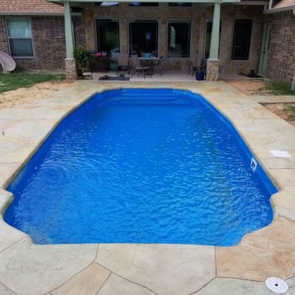 A large blue swimming pool is in the backyard of a house.