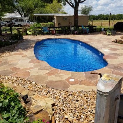 A large blue swimming pool is surrounded by rocks and a patio.